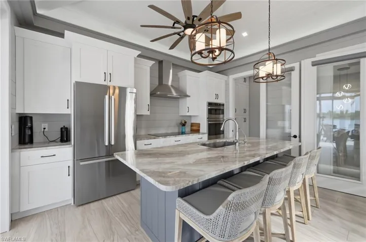 Kitchen with stainless steel appliances, light stone counters, an island with sink, a breakfast bar, and hanging light fixtures