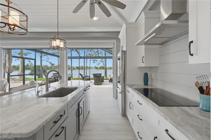 Dual tone kitchen with a large island with sink, stainless steel appliances, pendant lighting, light stone counters, and wood ceiling