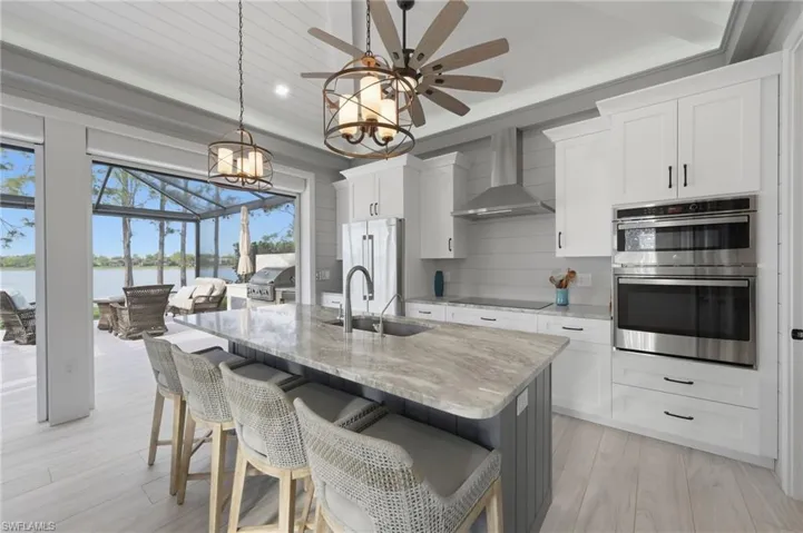 Kitchen with light wood-style floors, double oven, a breakfast bar, a center island with sink, and light stone countertops