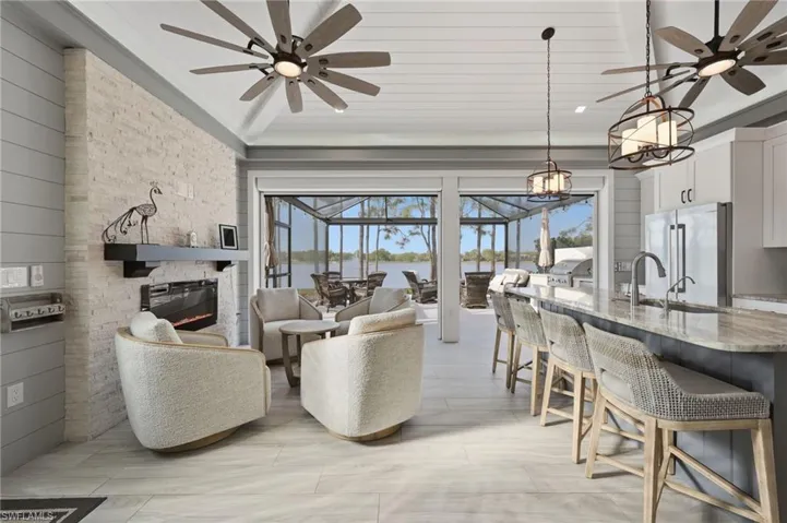 Living room with ceiling fan, a sunroom, plenty of natural light, a stone fireplace, and vaulted ceiling