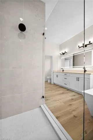Bathroom with dual vanity, toilet, a tile shower, and hardwood / wood-style floors