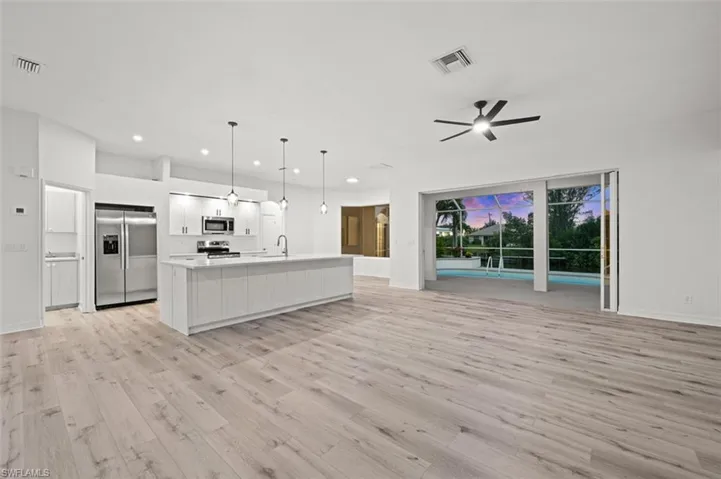 Kitchen with light hardwood / wood-style flooring, stainless steel appliances, a center island with sink, pendant lighting, and white cabinetry