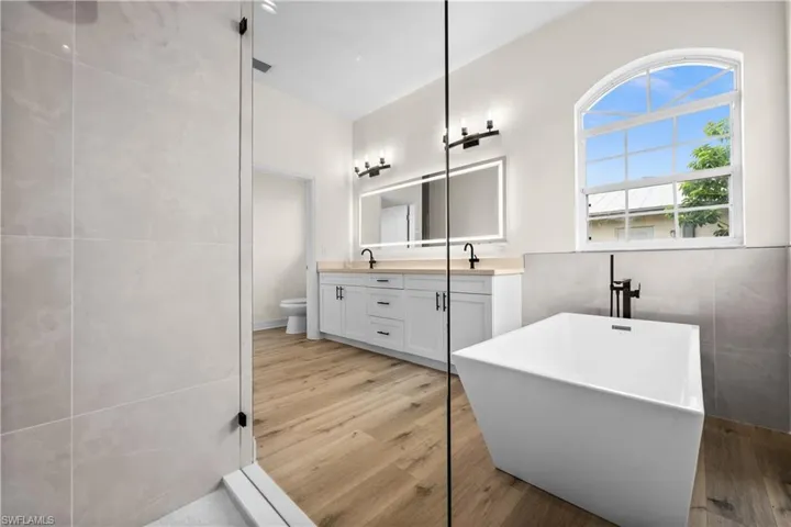 Bathroom featuring tile walls, a washtub, toilet, wood-type flooring, and double sink vanity