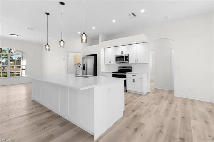 Kitchen with light wood-type flooring, a center island with sink, stainless steel appliances, white cabinets, and pendant lighting