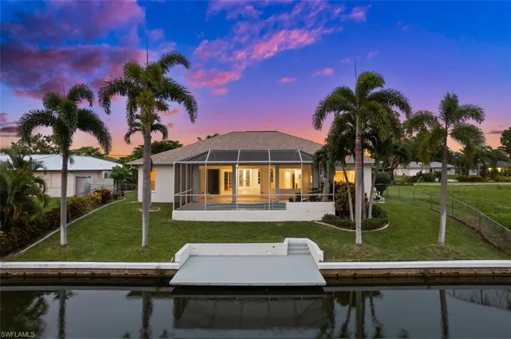 Back house at dusk with a patio, glass enclosure, a yard, and a fenced in pool