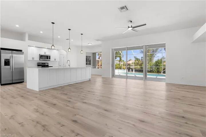 Kitchen with appliances with stainless steel finishes, light hardwood / wood-style floors, hanging light fixtures, and white cabinetry