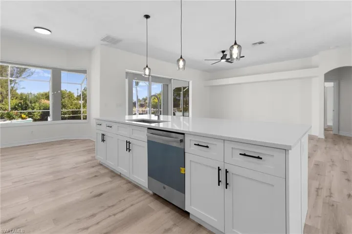 Kitchen featuring light hardwood / wood-style flooring, stainless steel dishwasher, decorative light fixtures, sink, and white cabinetry