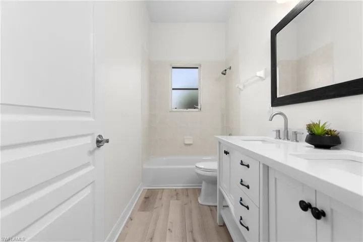 Full bathroom with double sink, tiled shower / bath, hardwood / wood-style floors, vanity with extensive cabinet space, and toilet