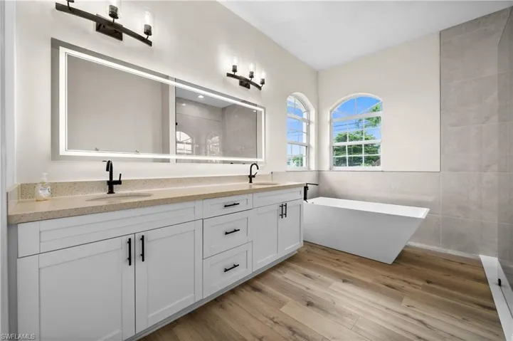 Bathroom featuring a tub, wood-type flooring, dual bowl vanity, and tile walls