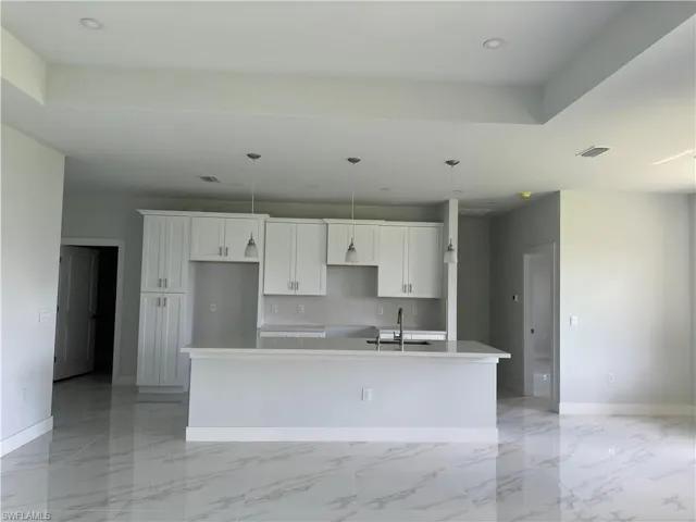 Kitchen with tasteful backsplash, light tile patterned floors, a center island with sink, white cabinets, and sink