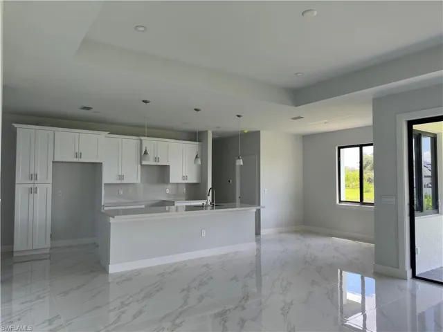 Kitchen with light tile patterned flooring, white cabinets, backsplash, a kitchen island with sink, and a raised ceiling