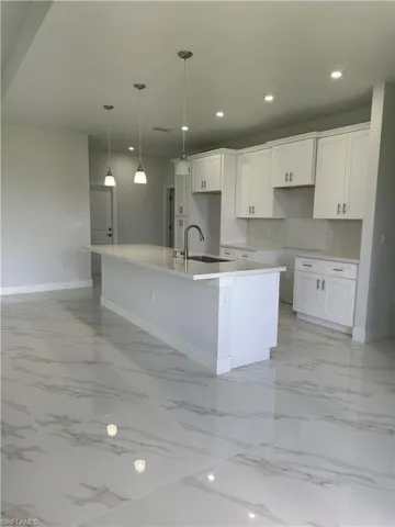 Kitchen with sink, pendant lighting, an island with sink, light tile patterned flooring, and white cabinetry