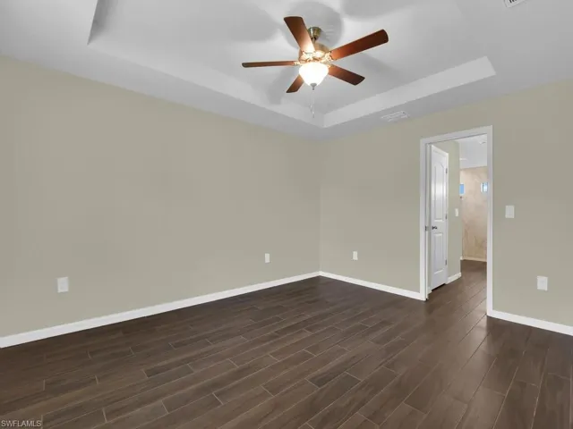 Unfurnished room with dark wood-type flooring, ceiling fan, and a tray ceiling