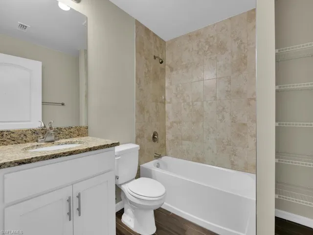Full bathroom with vanity, tiled shower / bath, hardwood / wood-style flooring, and toilet