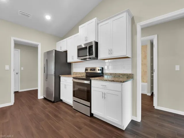 Kitchen featuring white cabinetry, lofted ceiling, tasteful backsplash, dark wood-type flooring, and appliances with stainless steel finishes