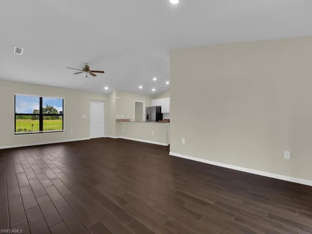 Unfurnished living room featuring dark wood-type flooring, ceiling fan, and vaulted ceiling