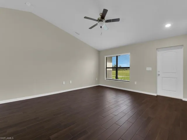 Empty room with dark hardwood / wood-style floors, vaulted ceiling, and ceiling fan