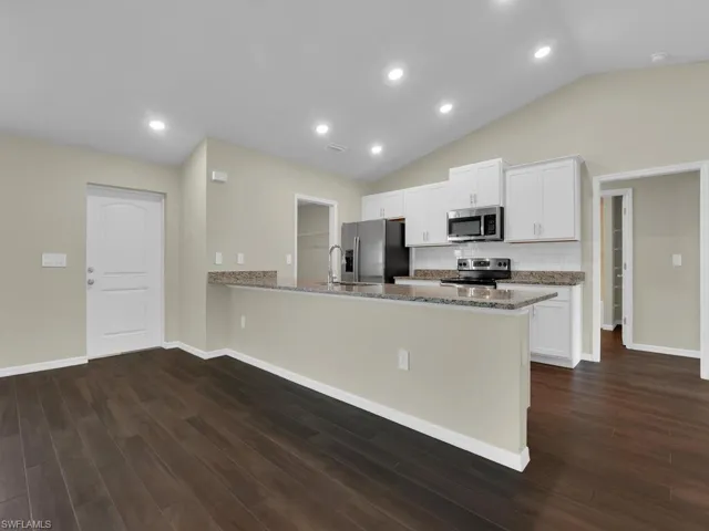 Kitchen with white cabinetry, dark hardwood / wood-style floors, kitchen peninsula, and stainless steel appliances