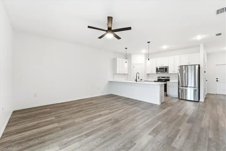 Kitchen featuring appliances with stainless steel finishes, open floor plan, white cabinetry, a peninsula, and hanging light fixtures