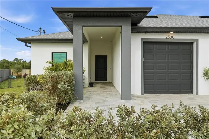 View of exterior entry featuring a shingled roof, stucco siding, and an attached garage