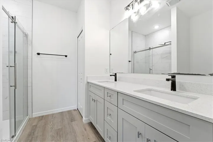 Full bathroom featuring double vanity, a marble finish shower, and light wood-type flooring