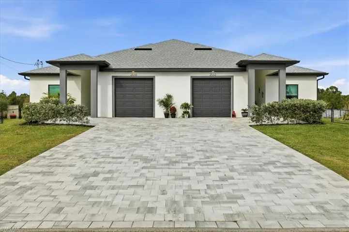 Prairie-style house with a front yard, decorative driveway, stucco siding, and a garage