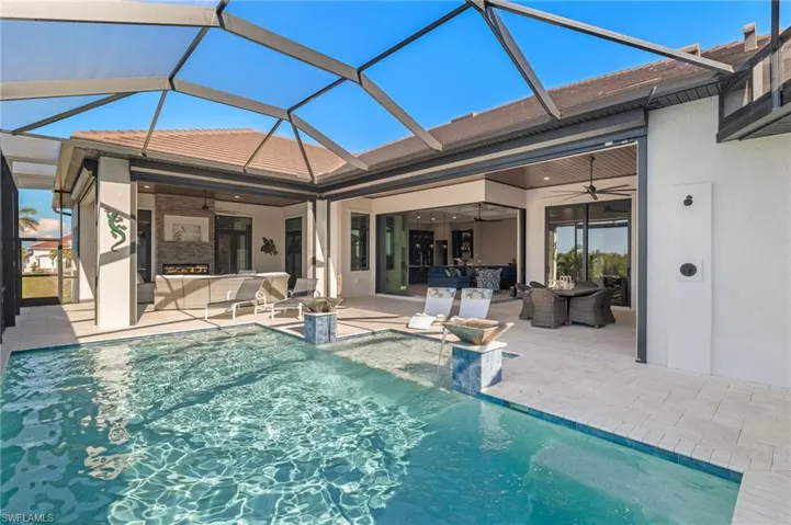 View of pool with ceiling fan, a patio, and a fully screened enclosure. View looking from the pool and lanai into the great room with 90 degree patio sliders open.