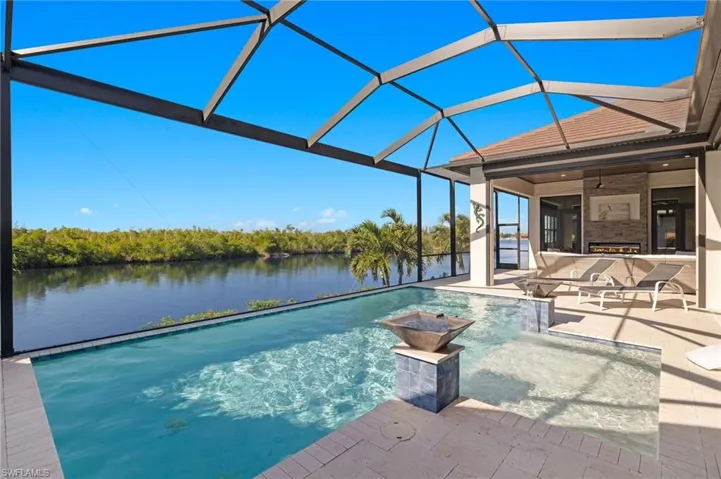 View of pool featuring ceiling fan, a patio area, a water view, a fully screened enclosure, and 2 waterfall fountains