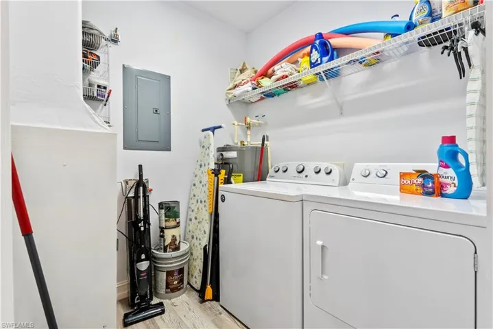 In-Unit Laundry room featuring electric panel, light hardwood / wood-style floors, water heater, and washer and clothes dryer