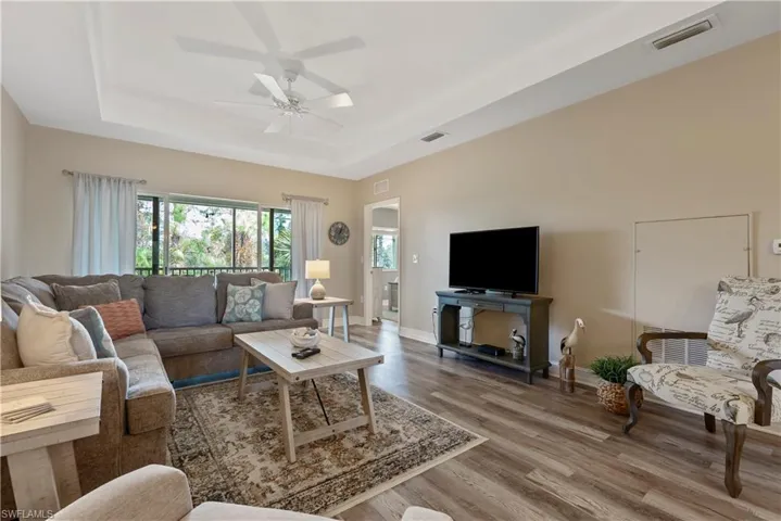 Living room with wood-type flooring, a tray ceiling, and ceiling fan
