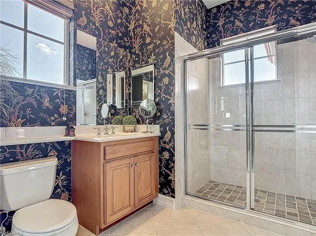 Bathroom featuring wallpapered walls, a shower stall, tile patterned floors, vanity, and toilet