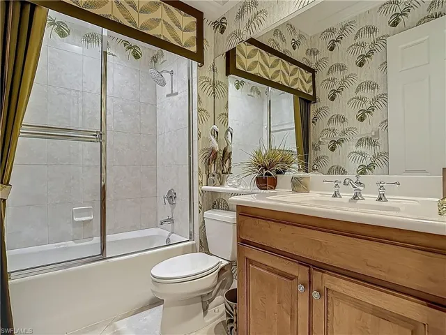 Bathroom featuring wallpapered walls, toilet, combined bath / shower with glass door, and vanity