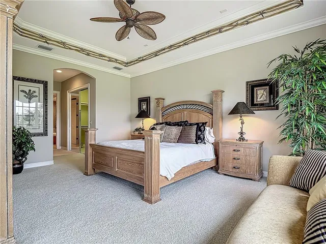 Carpeted bedroom featuring arched walkways, baseboards, crown molding, and ceiling fan