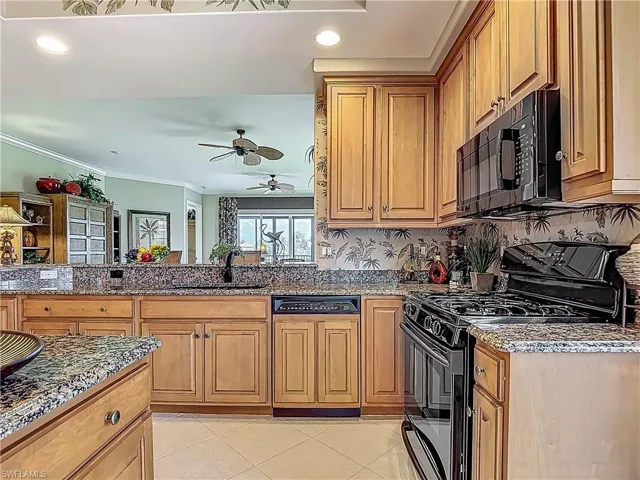 Kitchen featuring black appliances, a sink, a ceiling fan, dark stone counters, and ornamental molding