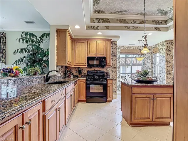 Kitchen featuring black appliances, a sink, ornamental molding, dark stone countertops, and a raised ceiling