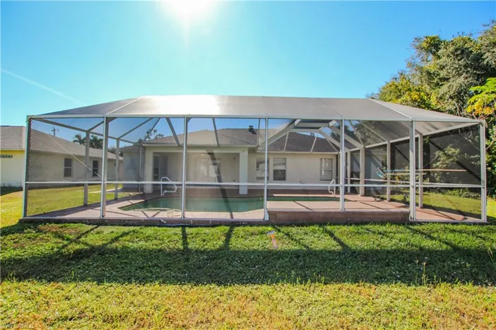 Rear view of house featuring an outdoor pool, a sunroom, glass enclosure, a yard, and a patio