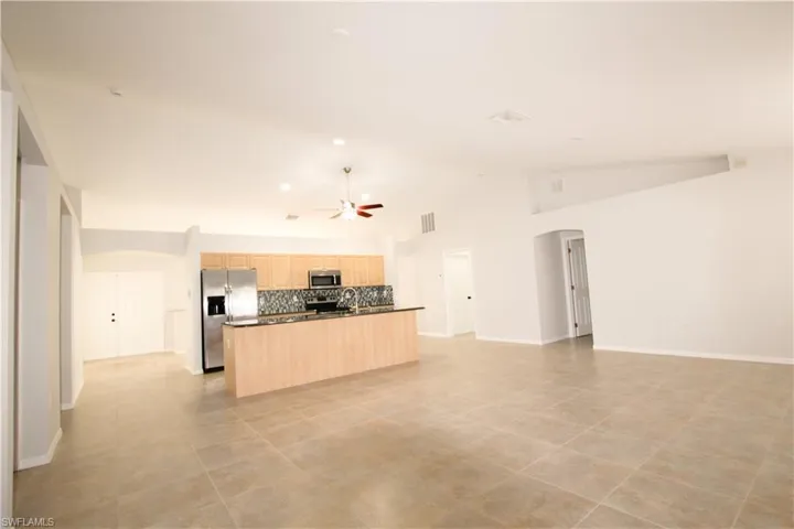 Kitchen with dark countertops, open floor plan, light brown cabinets, appliances with stainless steel finishes, and a center island with sink