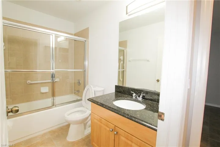 Bathroom with vanity, bath / shower combo with glass door, and light tile patterned floors