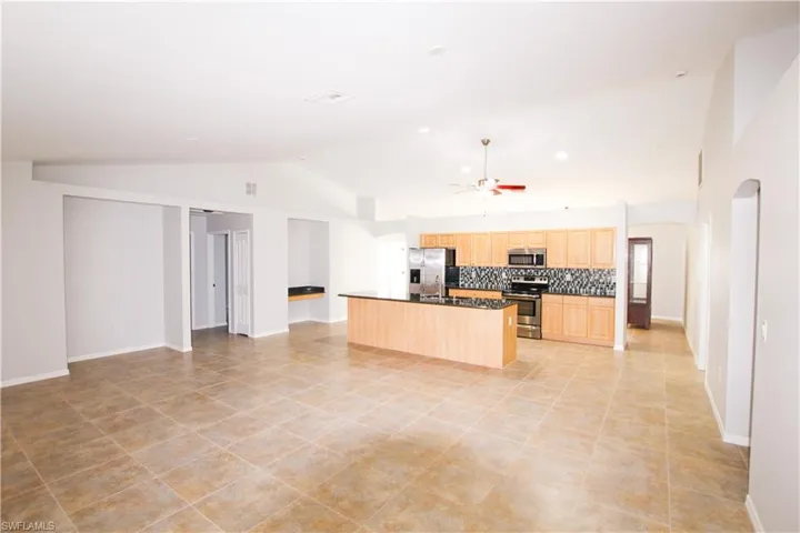 Kitchen featuring arched walkways, open floor plan, stainless steel appliances, light brown cabinets, and high vaulted ceiling