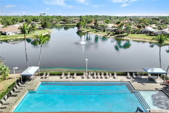 Community pool featuring a patio area, a lake view with water fountain and a residential background