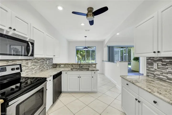 Kitchen featuring stainless steel appliances, decorative backsplash, white cabinetry, a peninsula, and granite counters