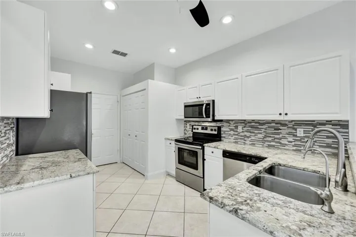 Kitchen with white cabinetry, stainless steel appliances, granite countertops, decorative backsplash, recessed lighting and light tile floors
