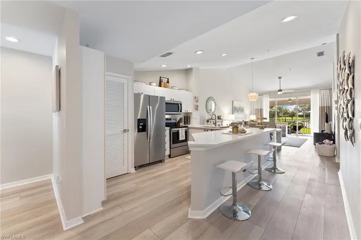 Kitchen with stainless steel appliances, a peninsula, a kitchen bar, vaulted ceiling, LVT floors, quartz countertops