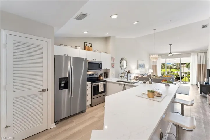 Kitchen with stainless steel appliances, a peninsula, a kitchen bar, vaulted ceiling, LVT floors, quartz countertops