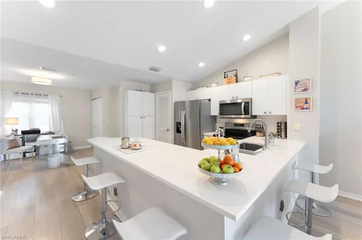 Kitchen with stainless steel appliances, a peninsula, a kitchen bar, vaulted ceiling, LVT floors, quartz countertops