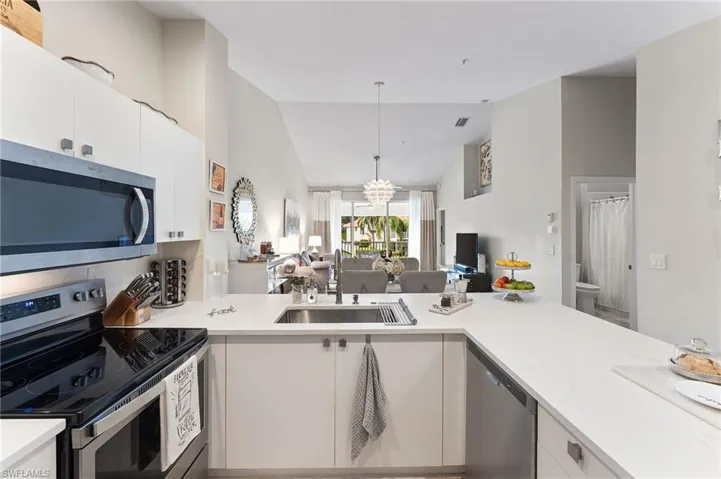 Kitchen with stainless steel appliances, a peninsula, a kitchen bar, vaulted ceiling, LVT floors, quartz countertops