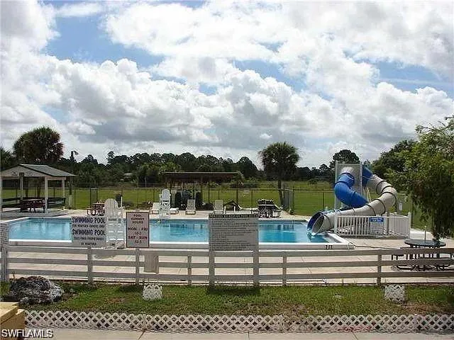 Community pool with a water slide, fence, and a patio area