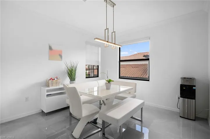 Dining area featuring a contemporary linear chandelier, large window with roller shade, and polished tile flooring
