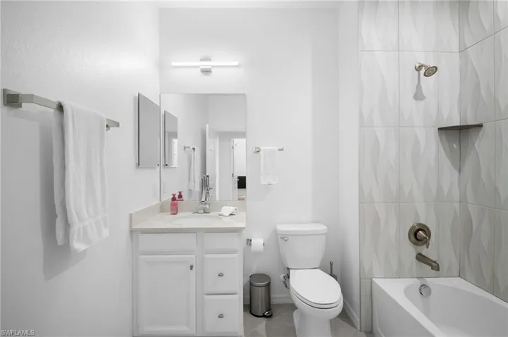 Contemporary bathroom featuring a single vanity with stone-finish countertop, white cabinetry, and a sleek rectangular mirror