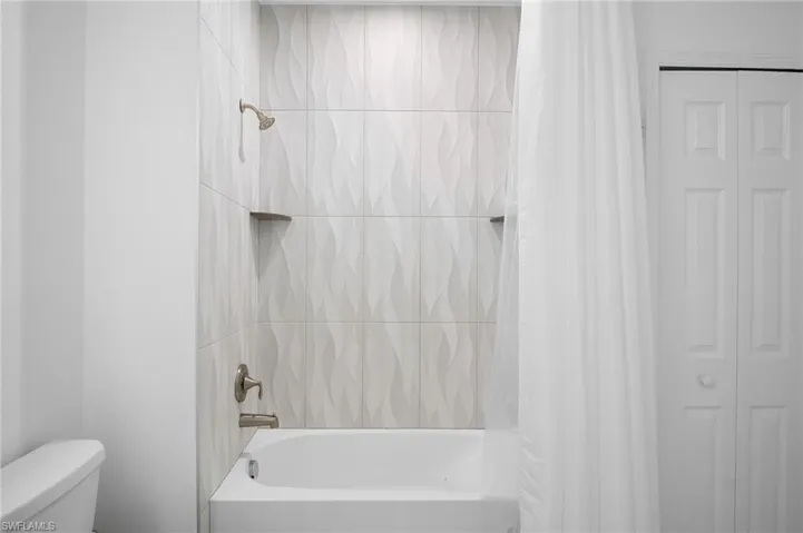 Bathtub and shower combination featuring textured white tile surround, two built-in corner shelves, and brushed nickel fixtures